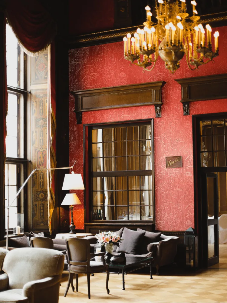 Luxurious red-walled lounge with a crystal chandelier, plush seating, and a vase of flowers.