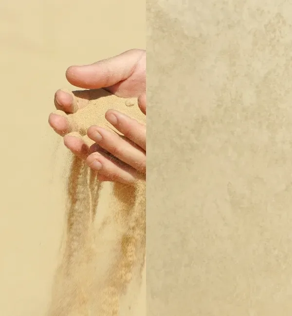 Hands hold fine sand, letting it trickle down against a textured, sandy background.