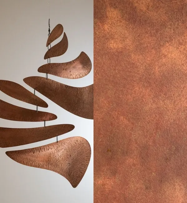 A copper mobile with curved, textured elements hangs against a white background next to a textured copper surface.