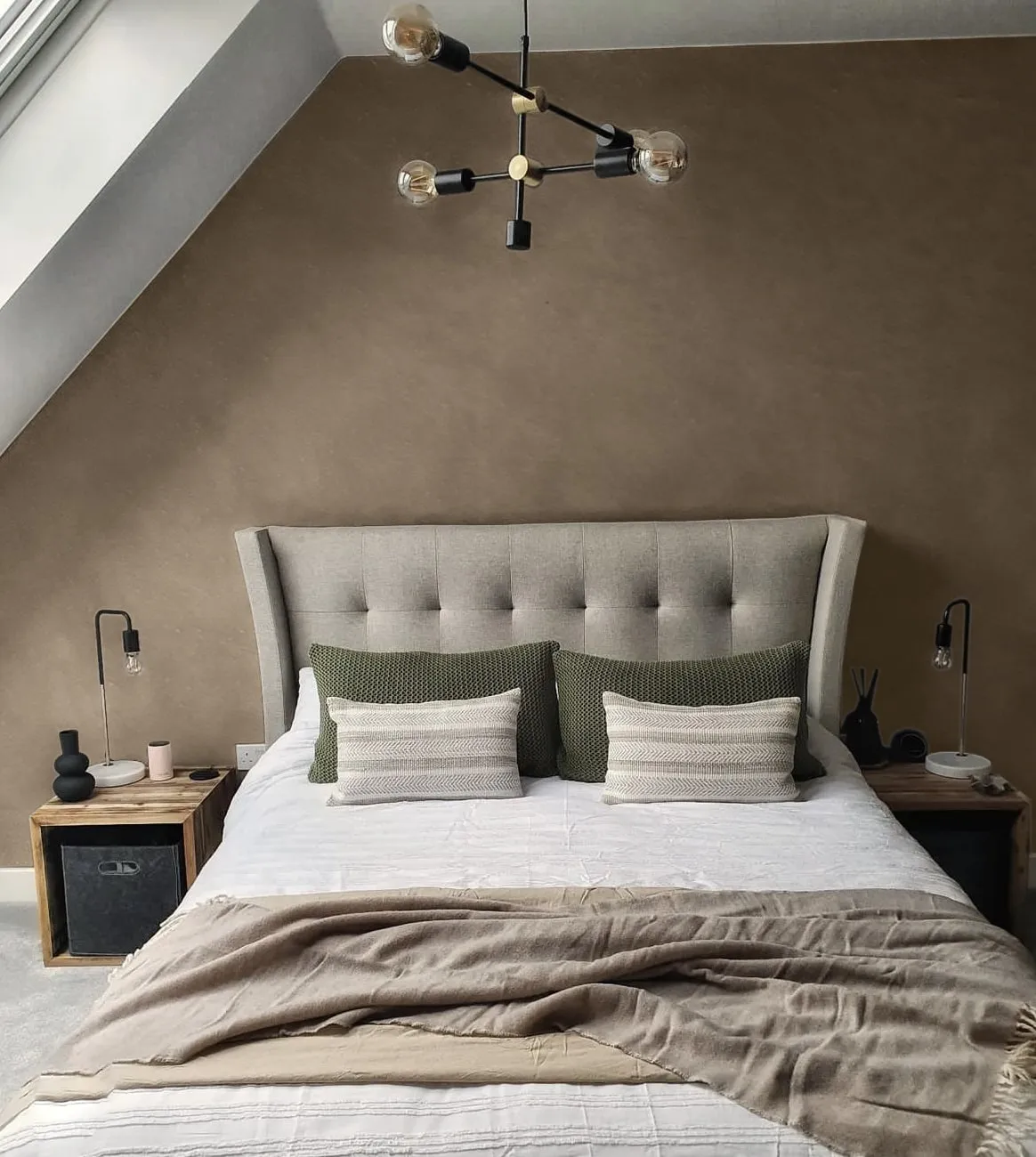 A cozy bedroom features a tufted headboard, layered pillows, and a textured throw blanket.