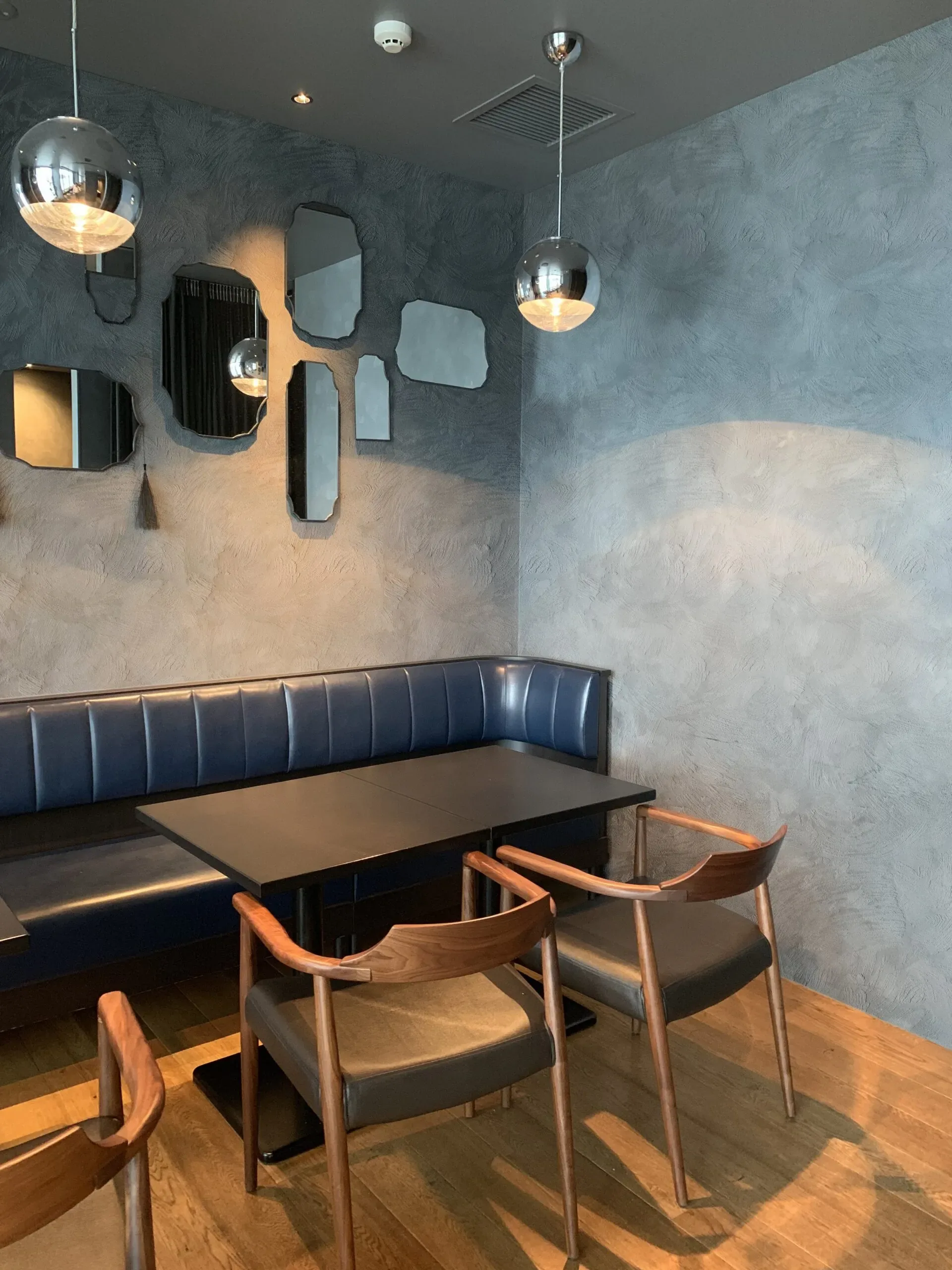 Modern dining area with a blue banquette, dark table, and wooden chairs against a textured gray wall.