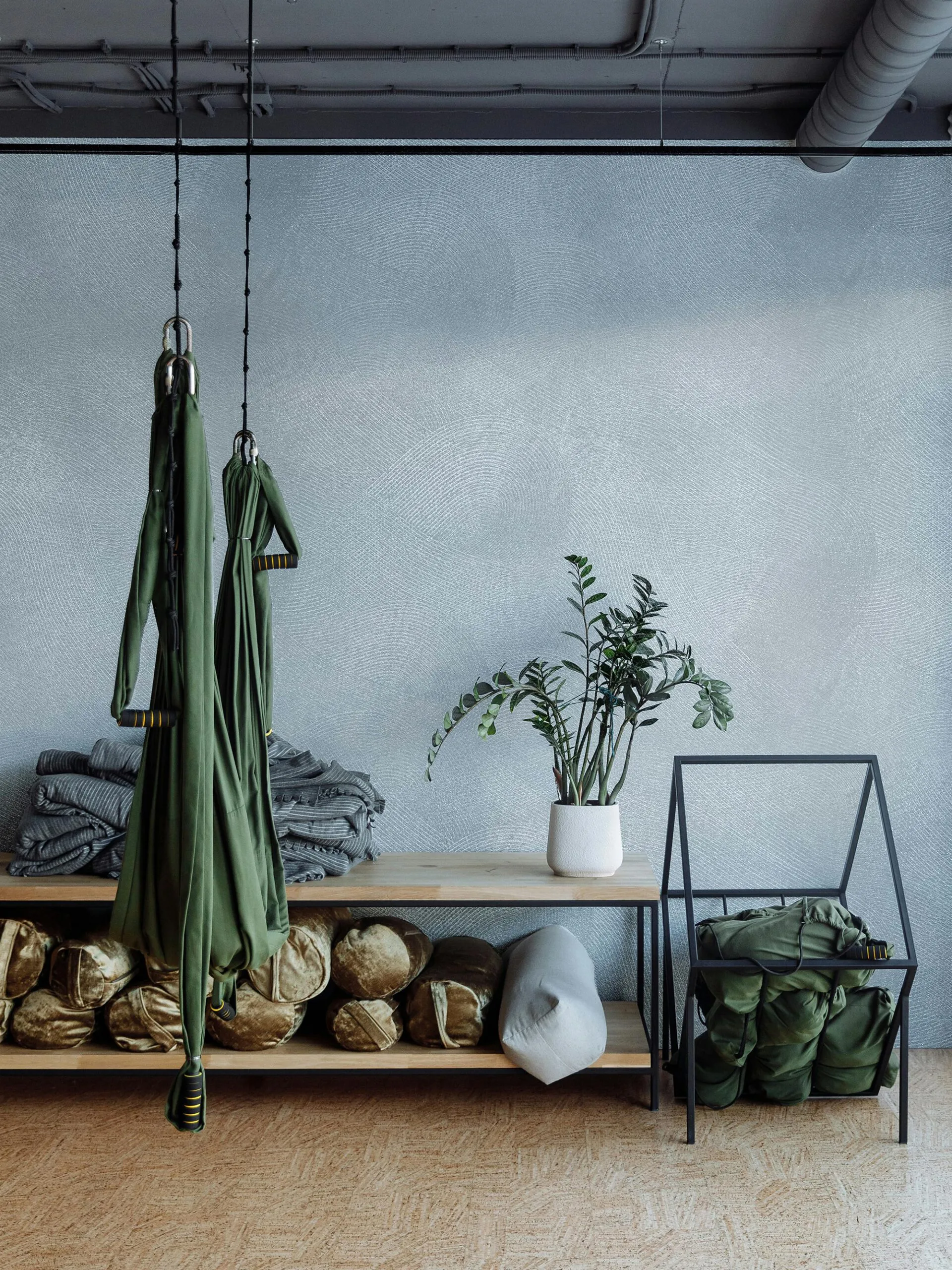 Green aerial yoga hammocks hang above shelves filled with bolsters and blankets in a studio.