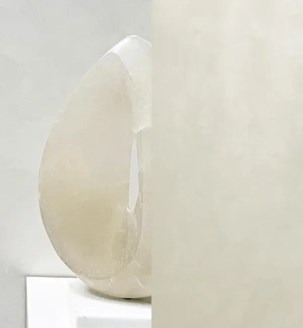 A translucent, polished marble sculpture rests on a white pedestal against a textured wall.