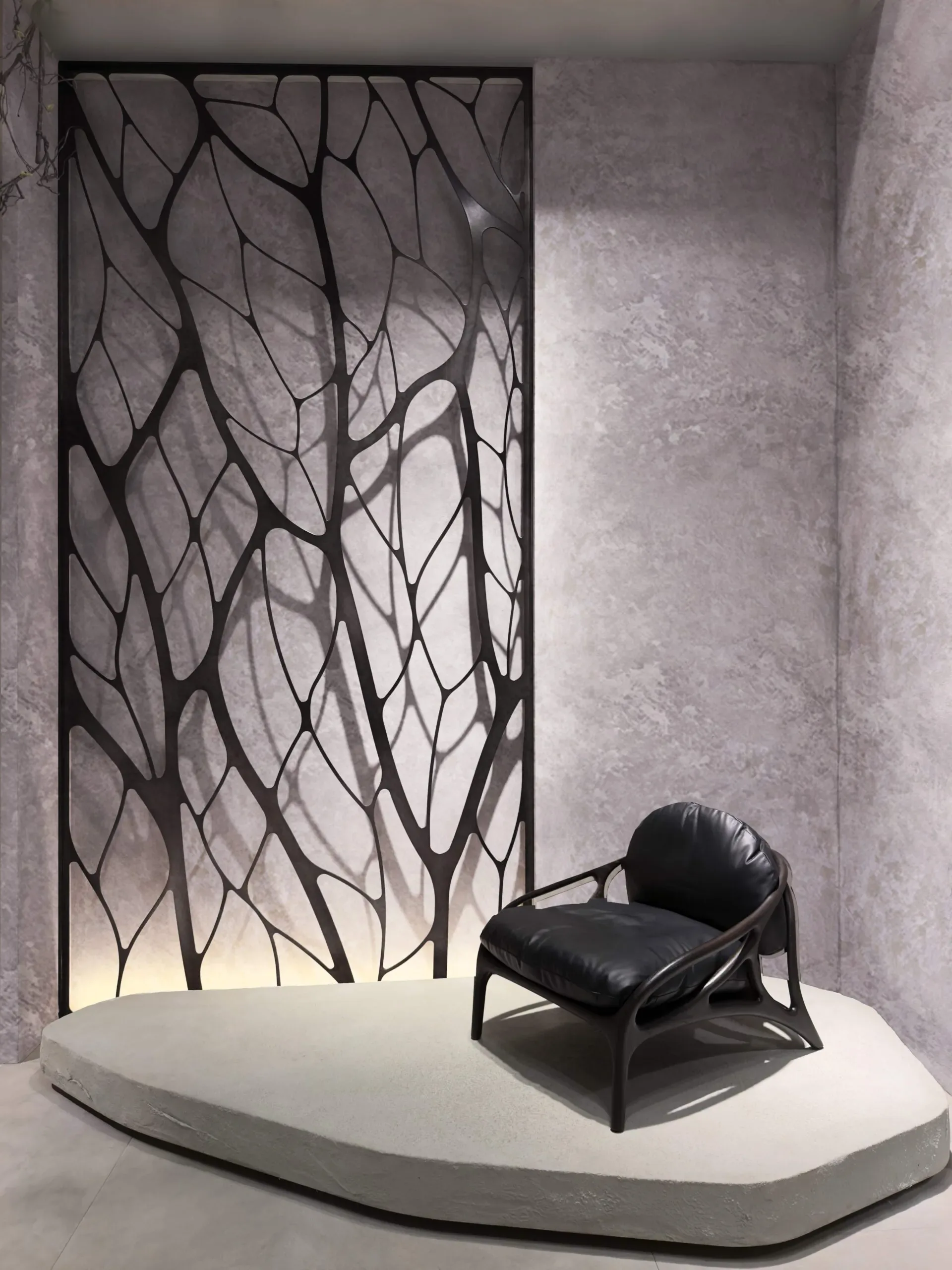A black leather armchair sits on a concrete pedestal before a decorative screen with a tree-like pattern.