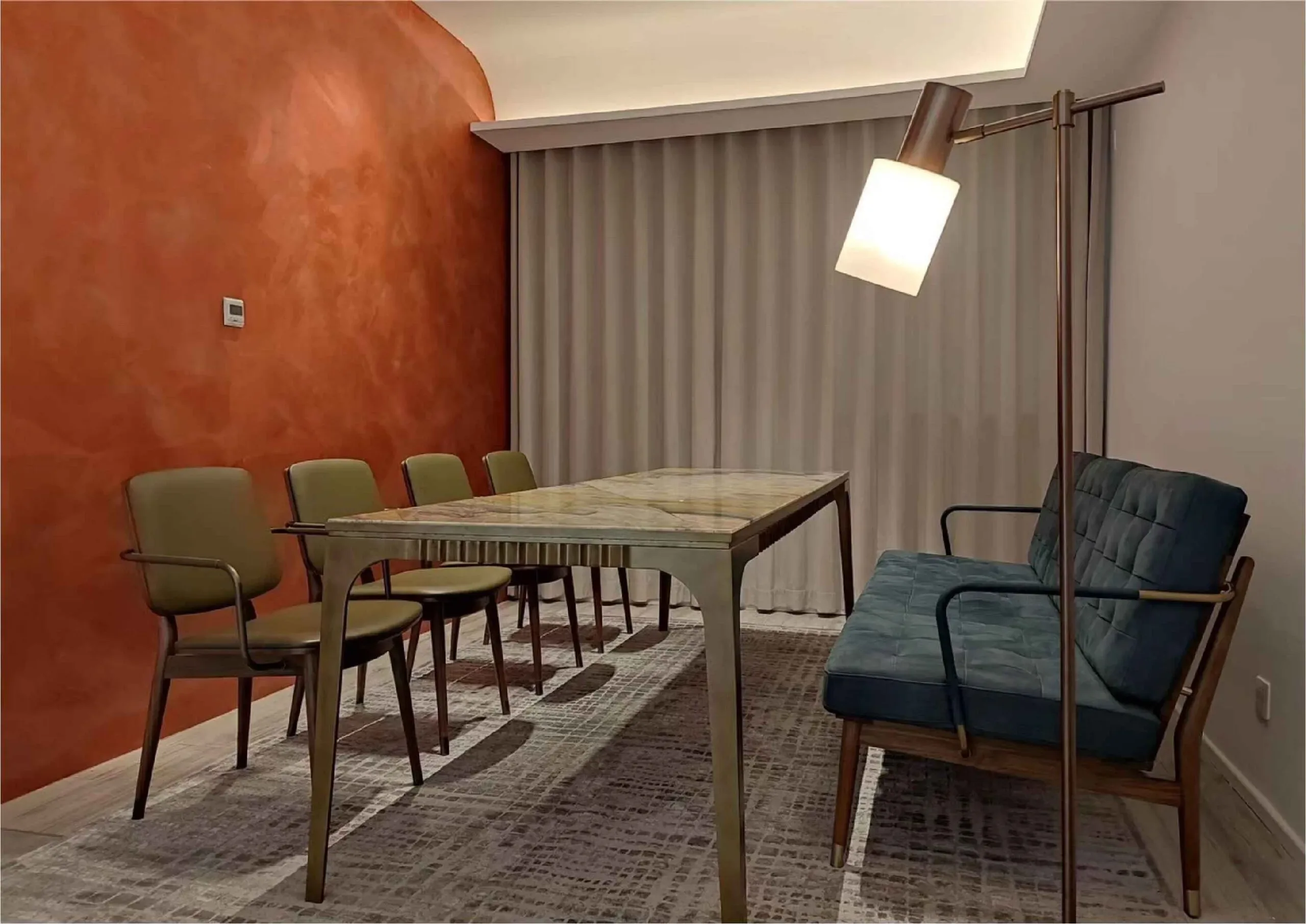 A dining room with a marble table, green chairs, and a blue sofa under a floor lamp.
