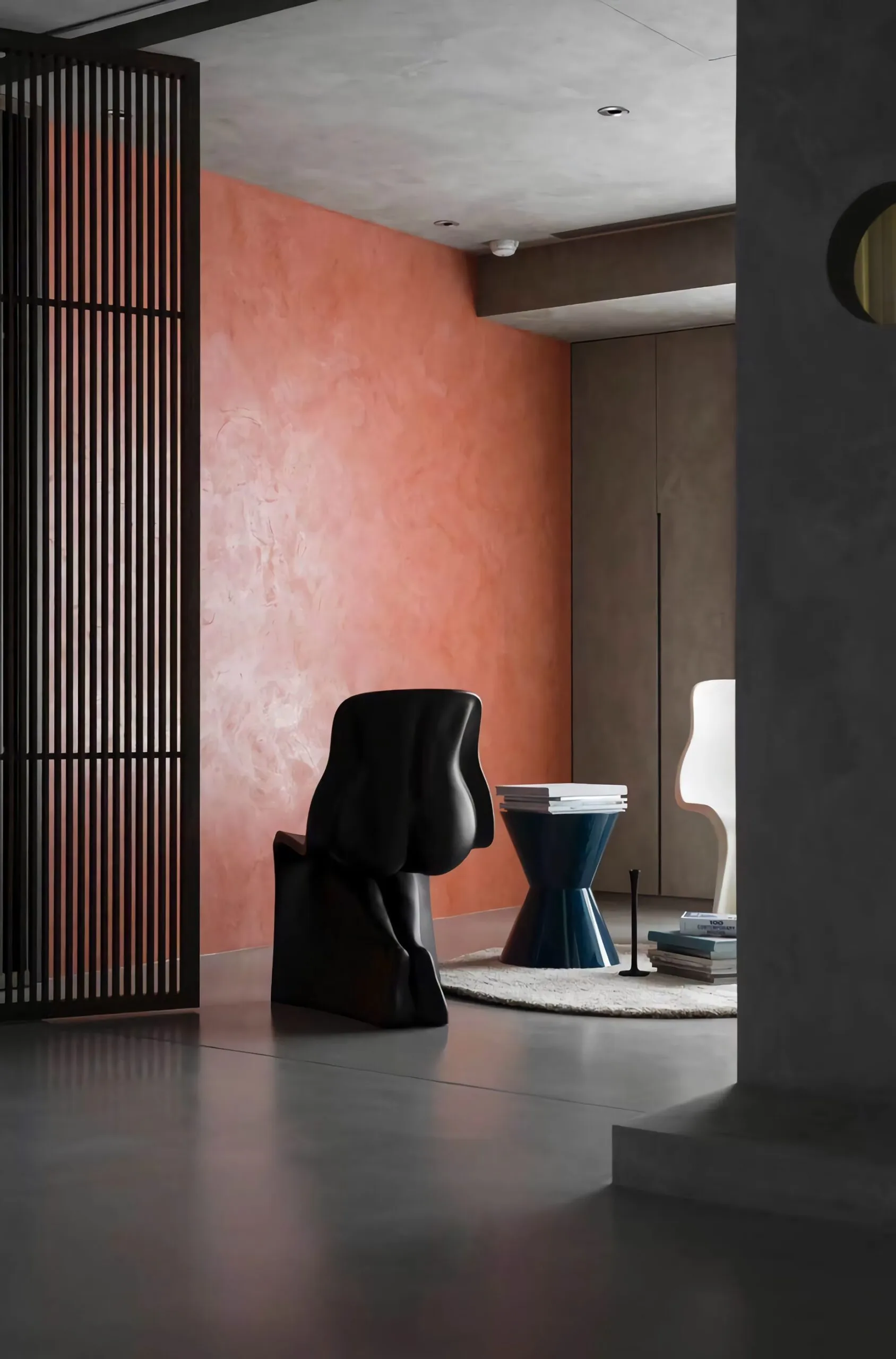 A black sculptural chair sits in a modern room with a coral-textured wall.